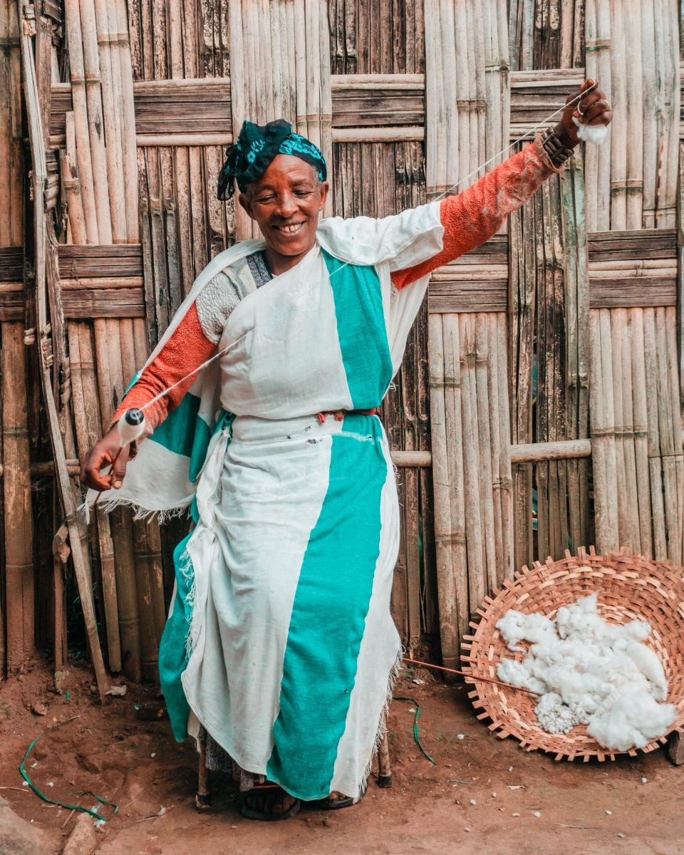 A cotton spinner in white and green outside her workshop